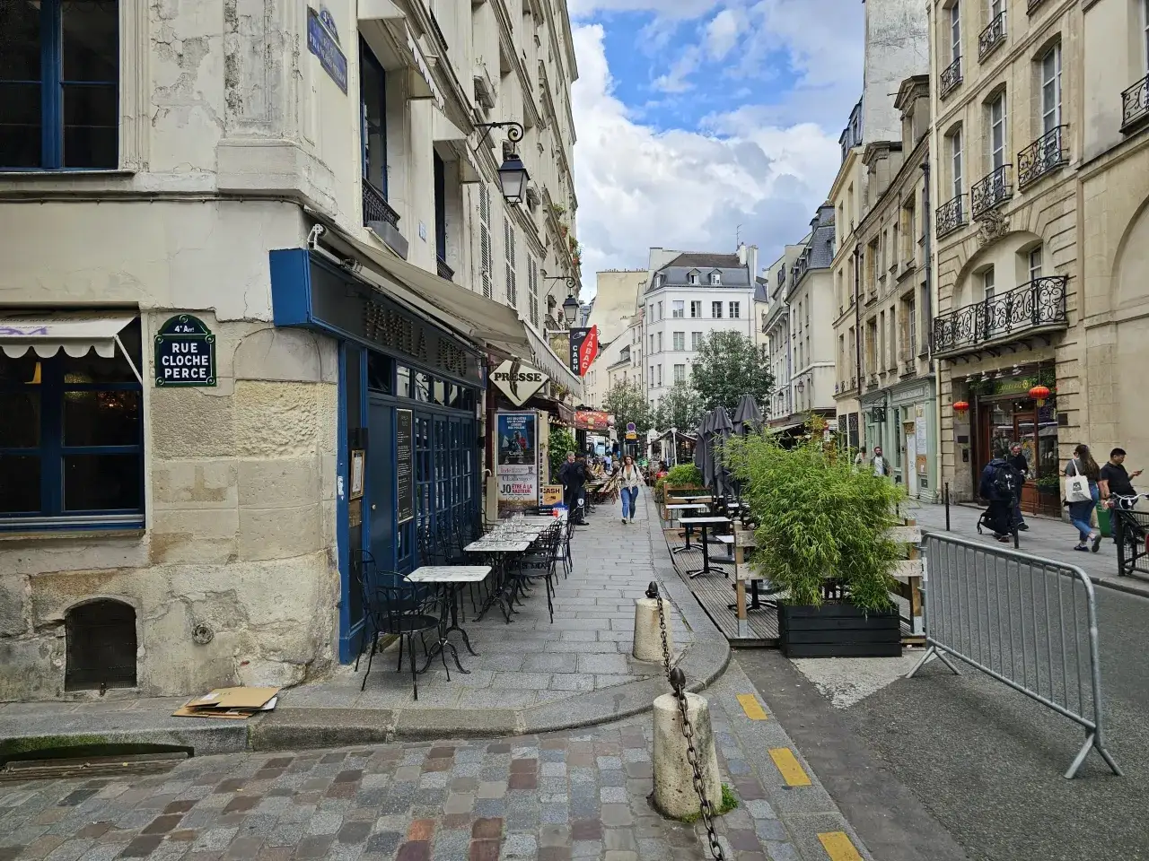 Ulica w paryskiej dzielnicy Le Marais z kawiarnianymi stolikami i budynkami.