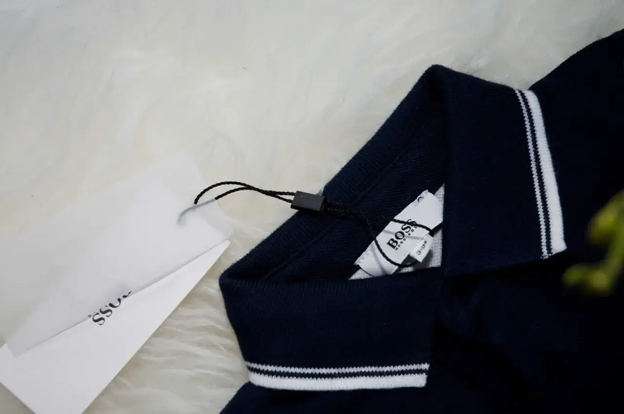 Granatowa koszulka polo z białymi paskami na kołnierzu i mankietach. Widoczna oryginalna metka Hugo Boss.