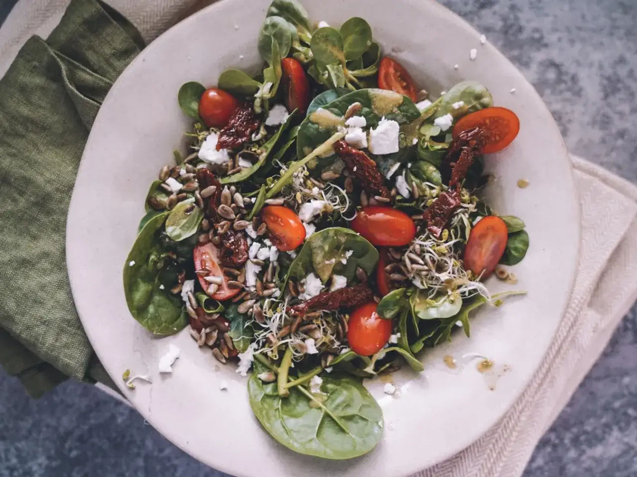 Kolorowa sałatka z suszonymi pomidorami, świeżymi pomidorkami, serem feta, kiełkami i nasionami słonecznika, polana sosem.