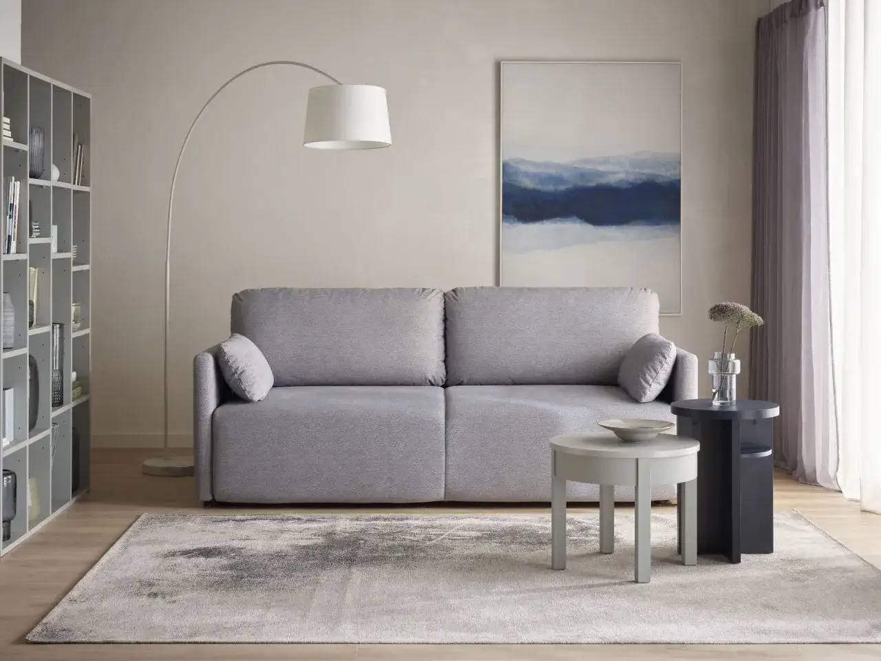 Przytulny pokój 15m2 z szarą kanapą, regałem i abstrakcyjnym obrazem.