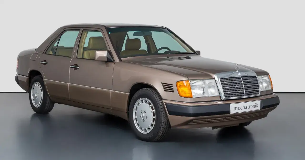 Brązowy Mercedes W124, klasyk z lat 80., prezentuje się elegancko na ciemnoszarym tle.