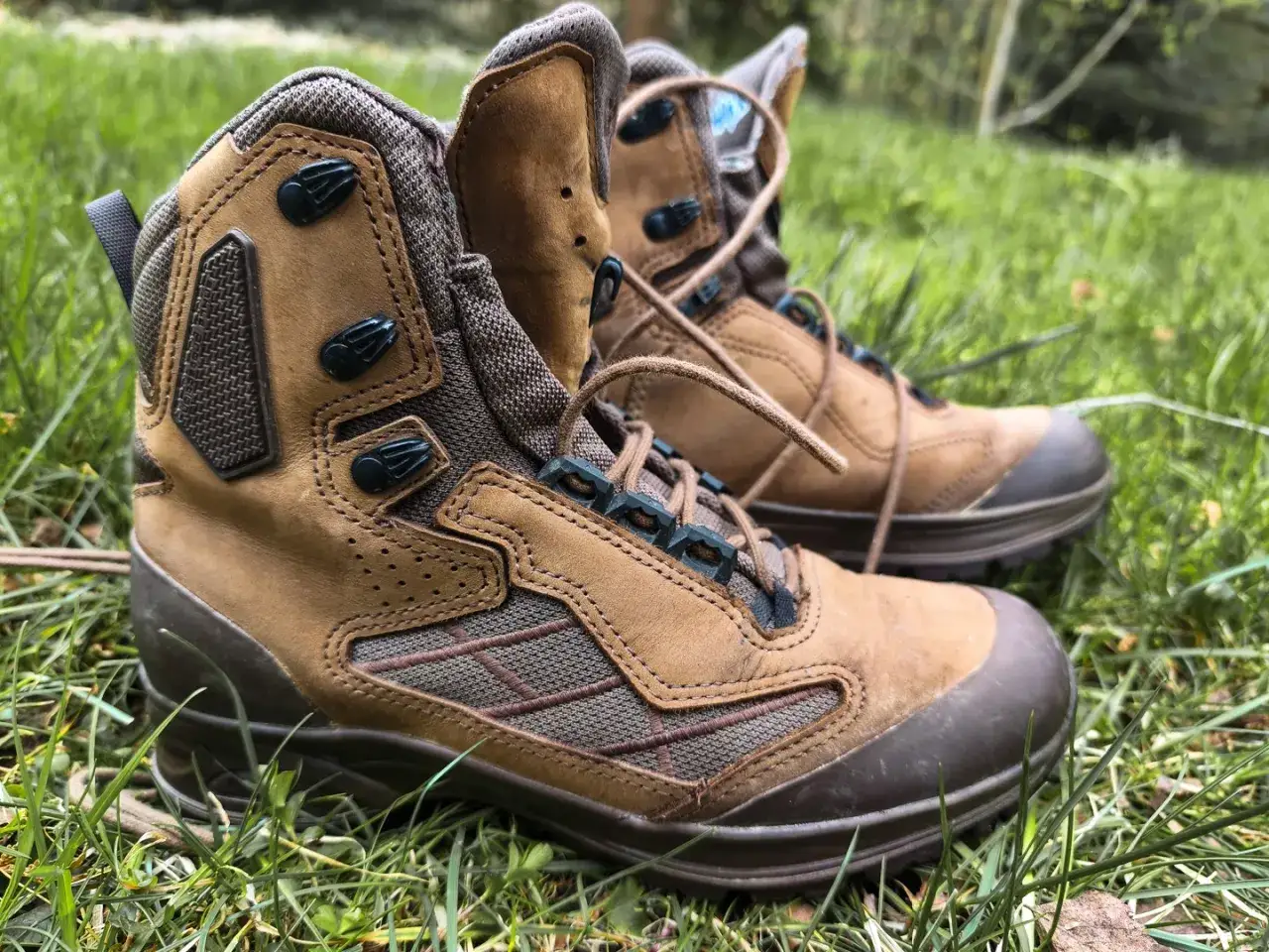 Brązowe buty trekkingowe na trawie. Nowe, ale już czuć, że buty trekkingowe obcierają pięty.