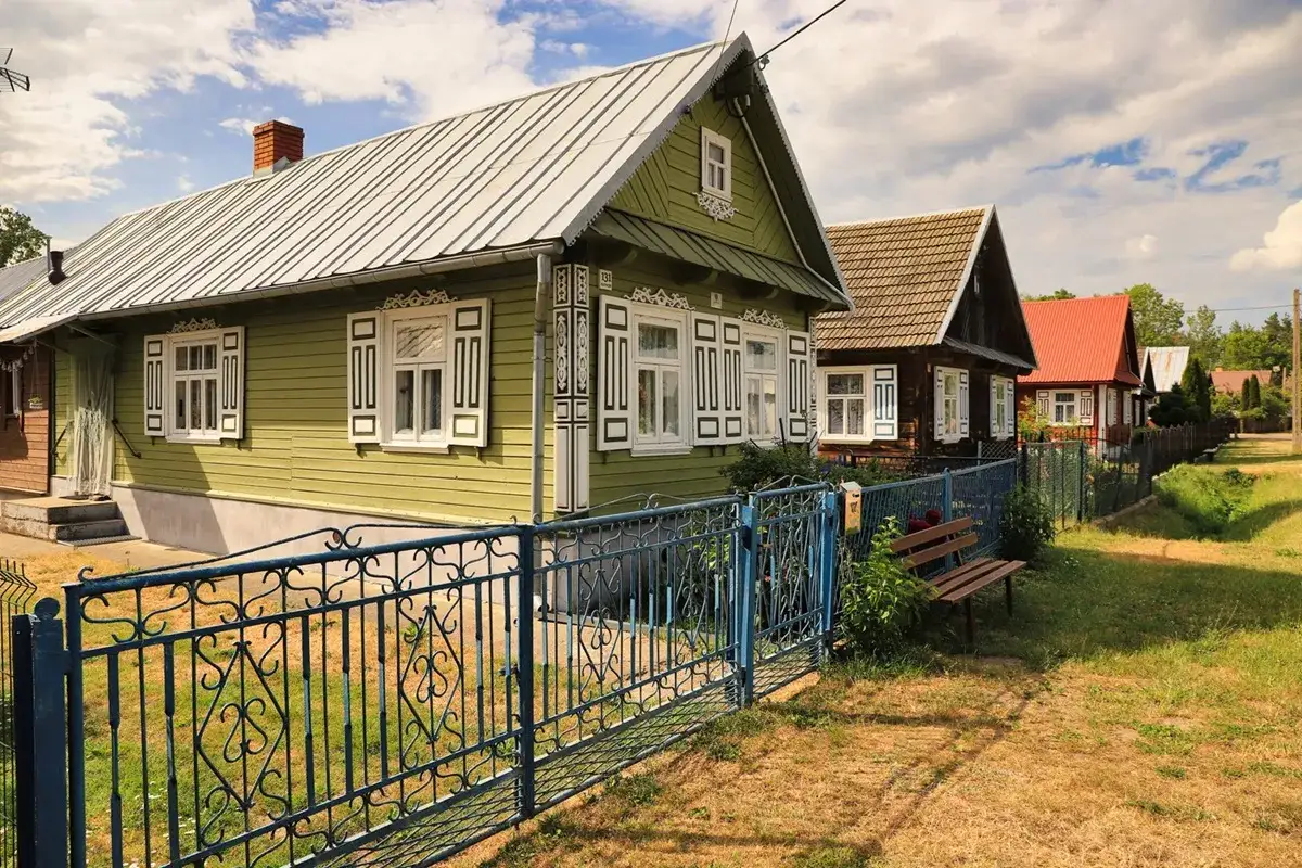 Urokliwe krajobrazy Podlasia: rzędy drewnianych domów z ozdobnymi okiennicami, niebieskie płoty i ławka w słońcu.