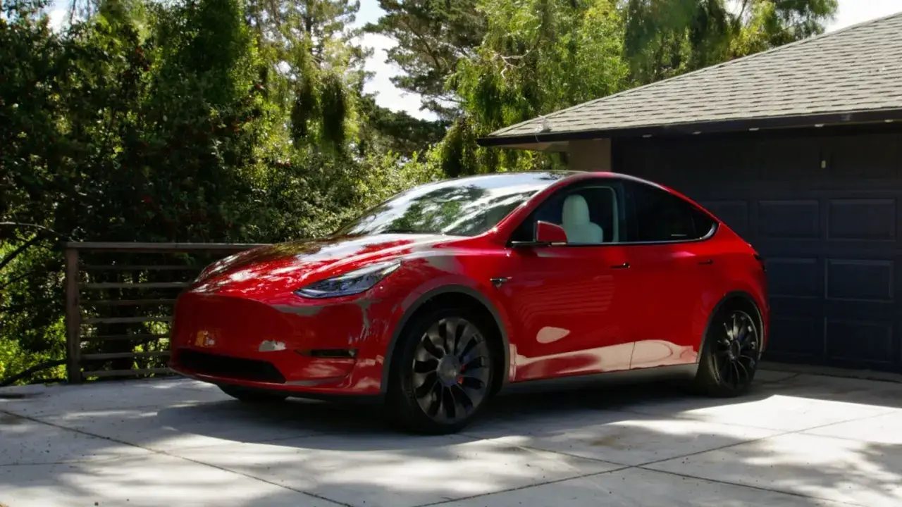 Czerwona Tesla Model Y na podjeździe przed garażem. Zastanawiasz się, ile kosztuje najnowsza Tesla?