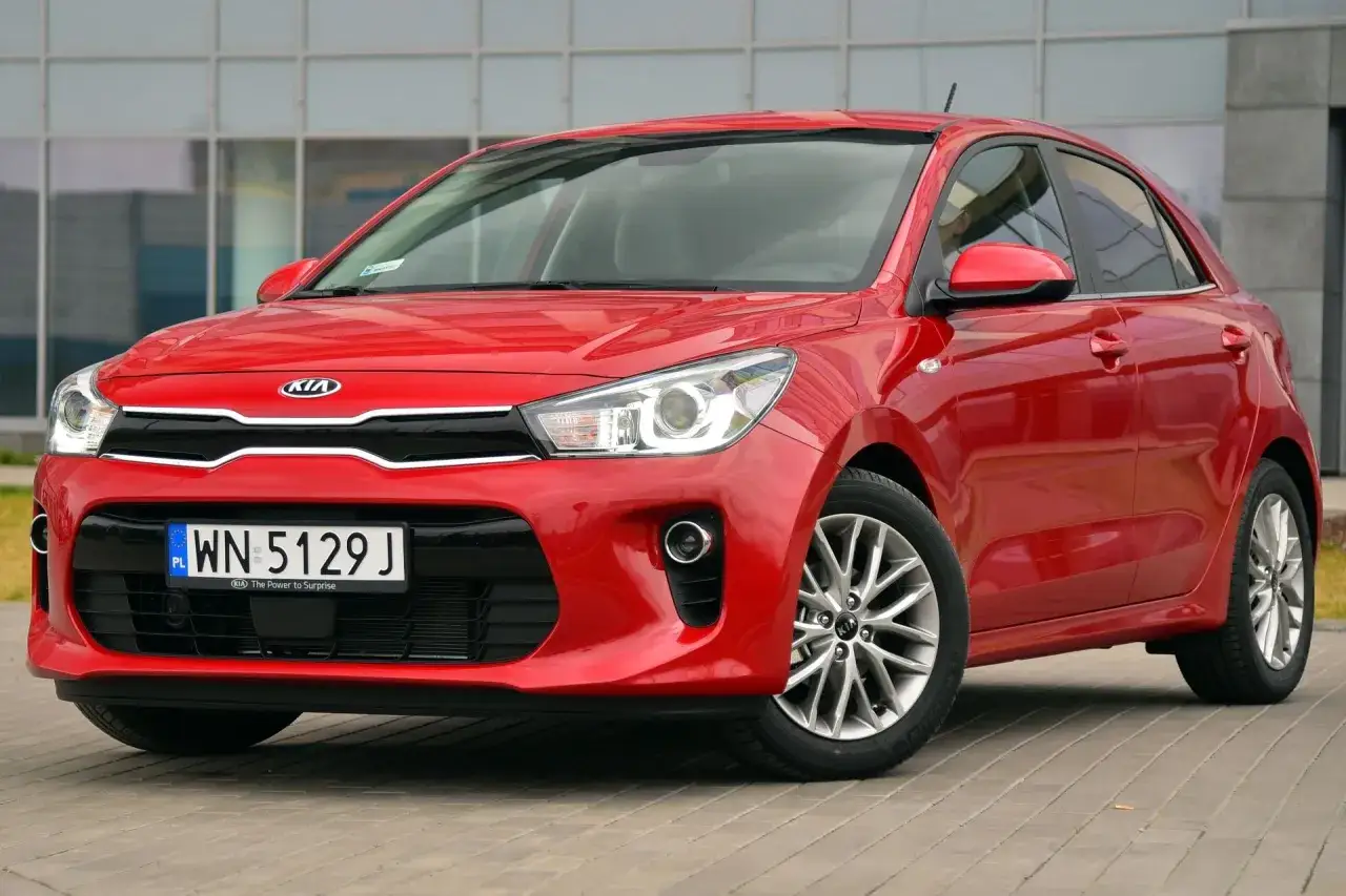 Czerwone Kia Rio z przodu. Widoczne światła pozycyjne w przednich reflektorach i na błotnikach.