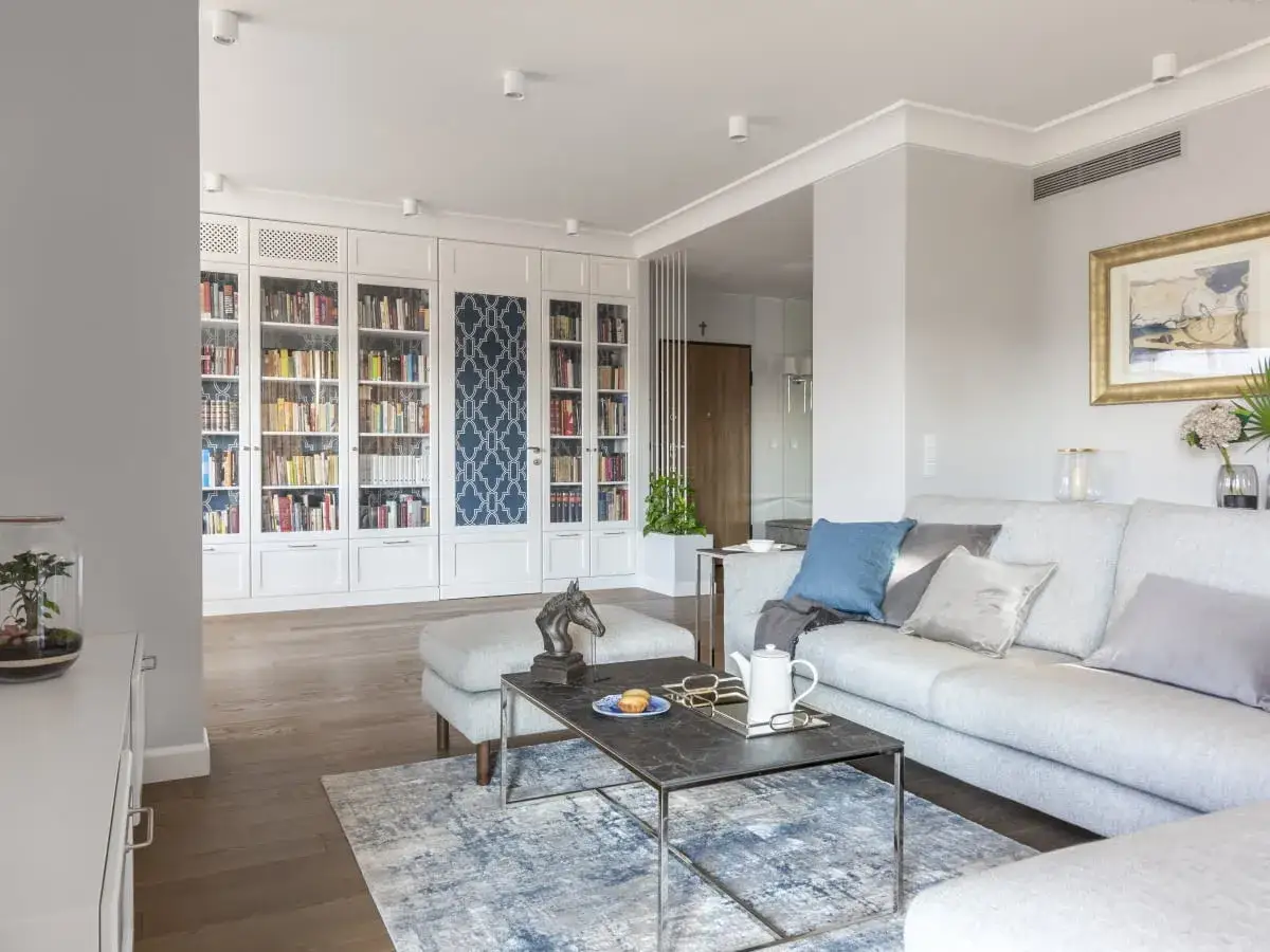 Elegancki salon w stylu nowojorskim z dużą biblioteczką, wygodną kanapą i dywanem w niebieskie wzory.