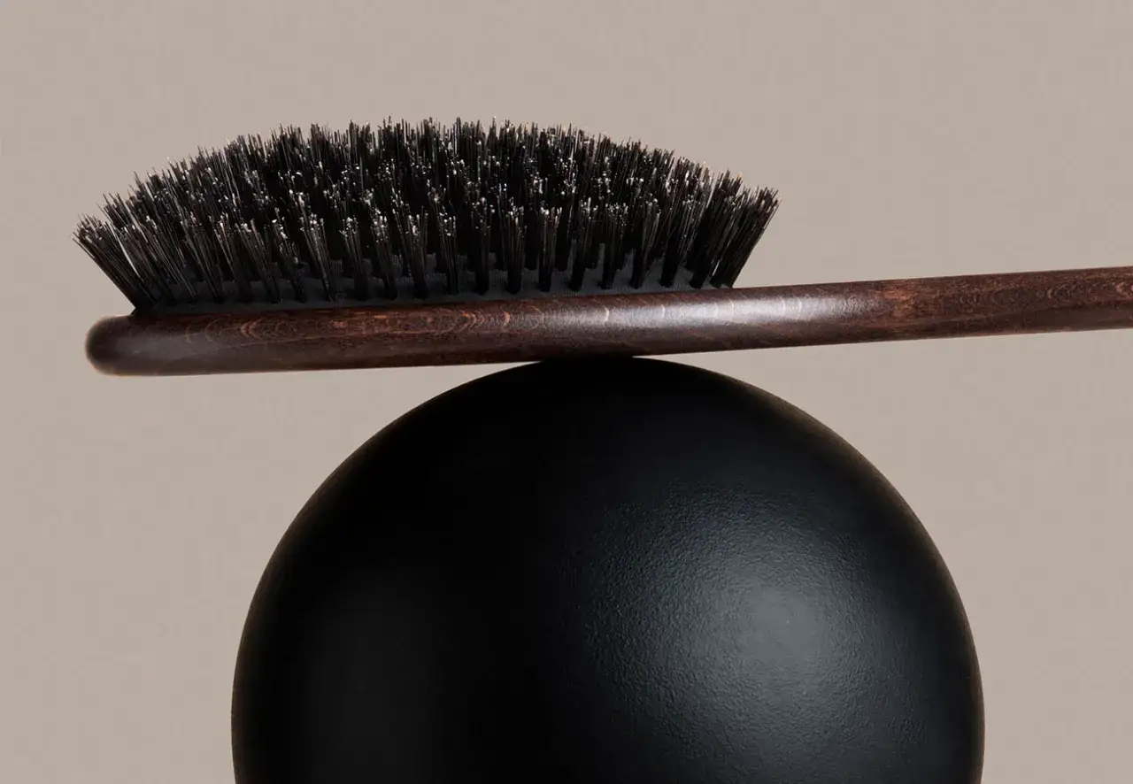 Elegancka, drewniana szczotka do włos&oacute;w z ciemnym włosiem, balansująca na czarnej kuli. Idealna do codziennej pielęgnacji.