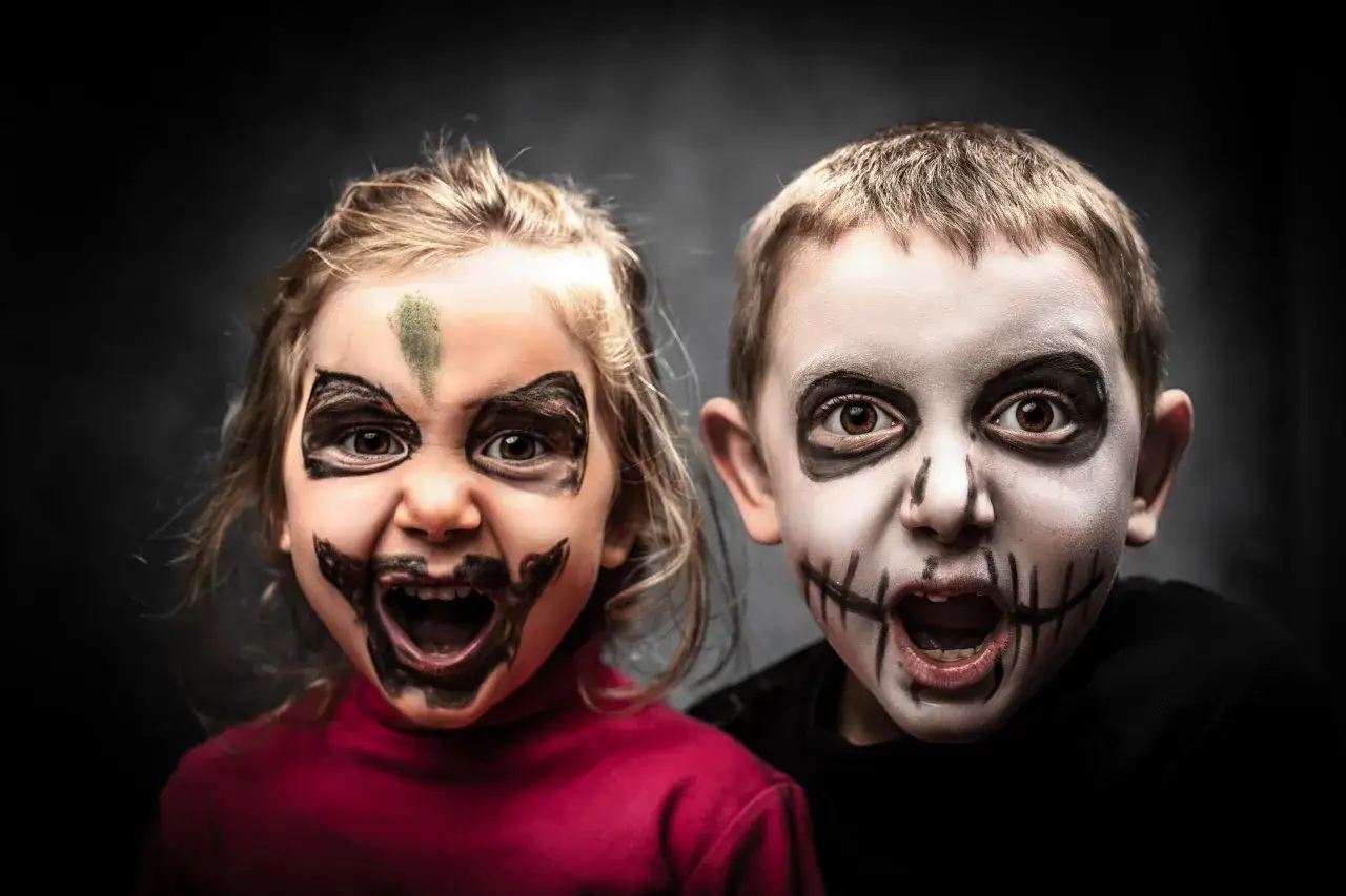 Dzieci z przerażającymi makijażami na Halloween. Chłopiec ma białą twarz z czarnymi szwami, dziewczynka zieloną plamę na czole i czarne wzory. Oto jak pomalować dziecko na Halloween!