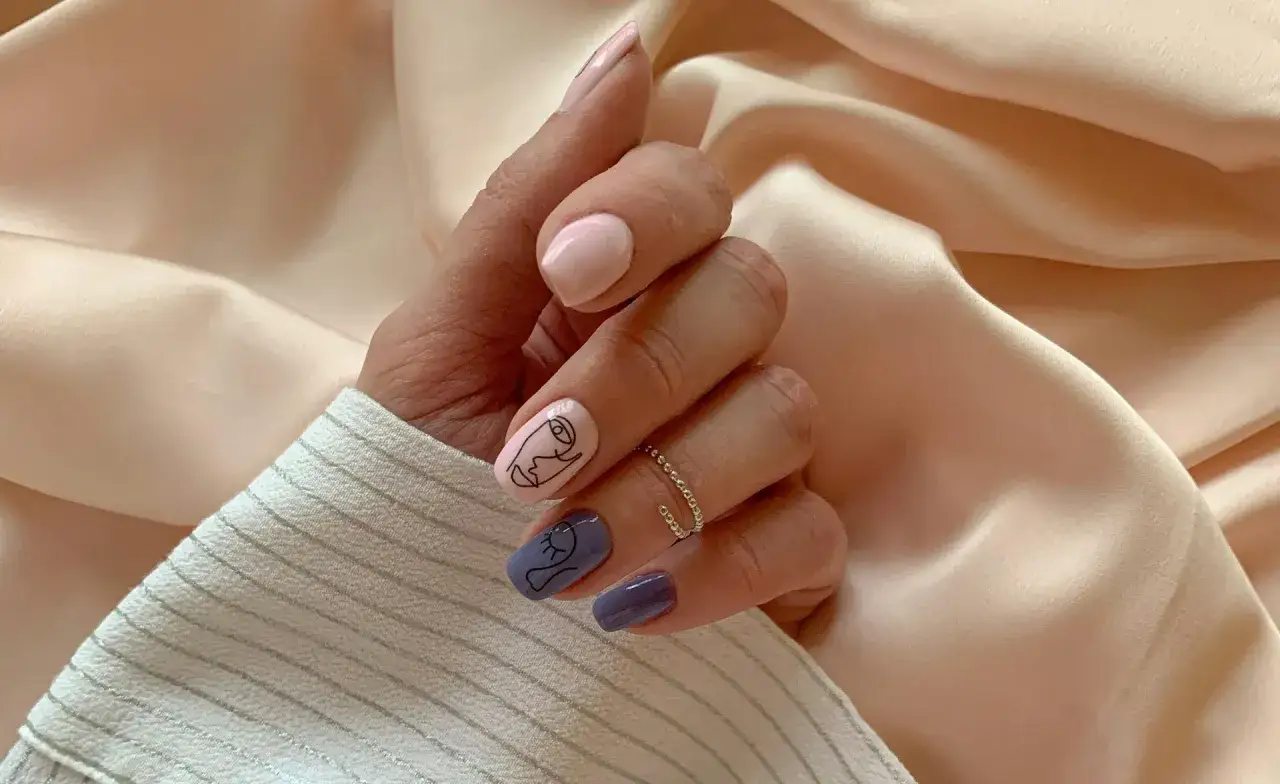 Dłoń z paznokciami hybrydowymi w pastelowych kolorach i rysunkami twarzy. Czy hybryda jest szkodliwa? Zadbaj o swoje dłonie.