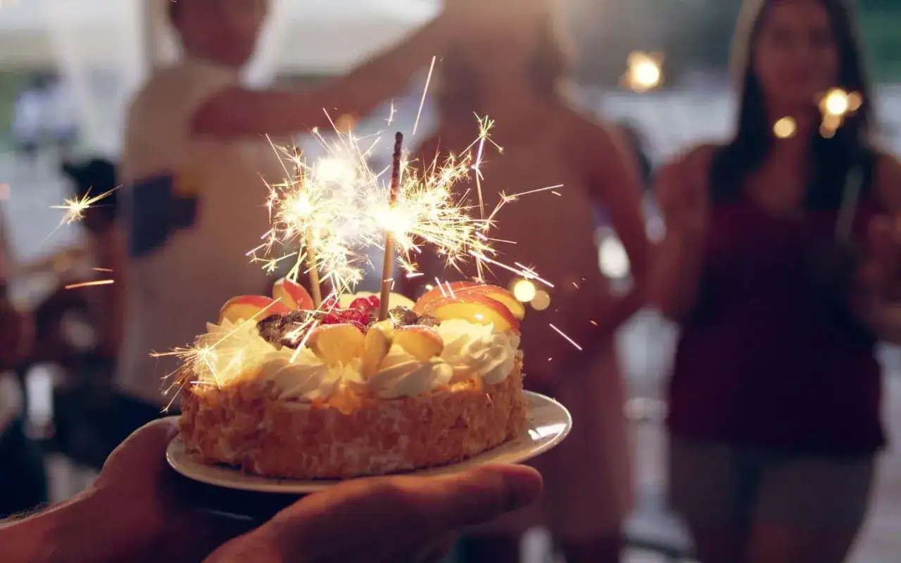 Tort urodzinowy z zimnymi ogniami, ozdobiony owocami i bitą śmietaną. Zastanawiasz się, ile kosztuje przyjęcie urodzinowe w restauracji?
