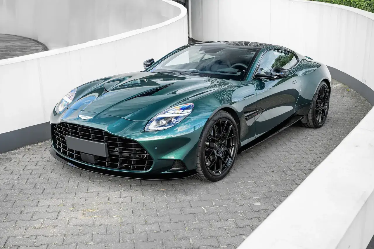 Zielony Aston Martin na tle białej, zakrzywionej ściany. Sprawdź, jaka jest aston martin cena tego cacka.