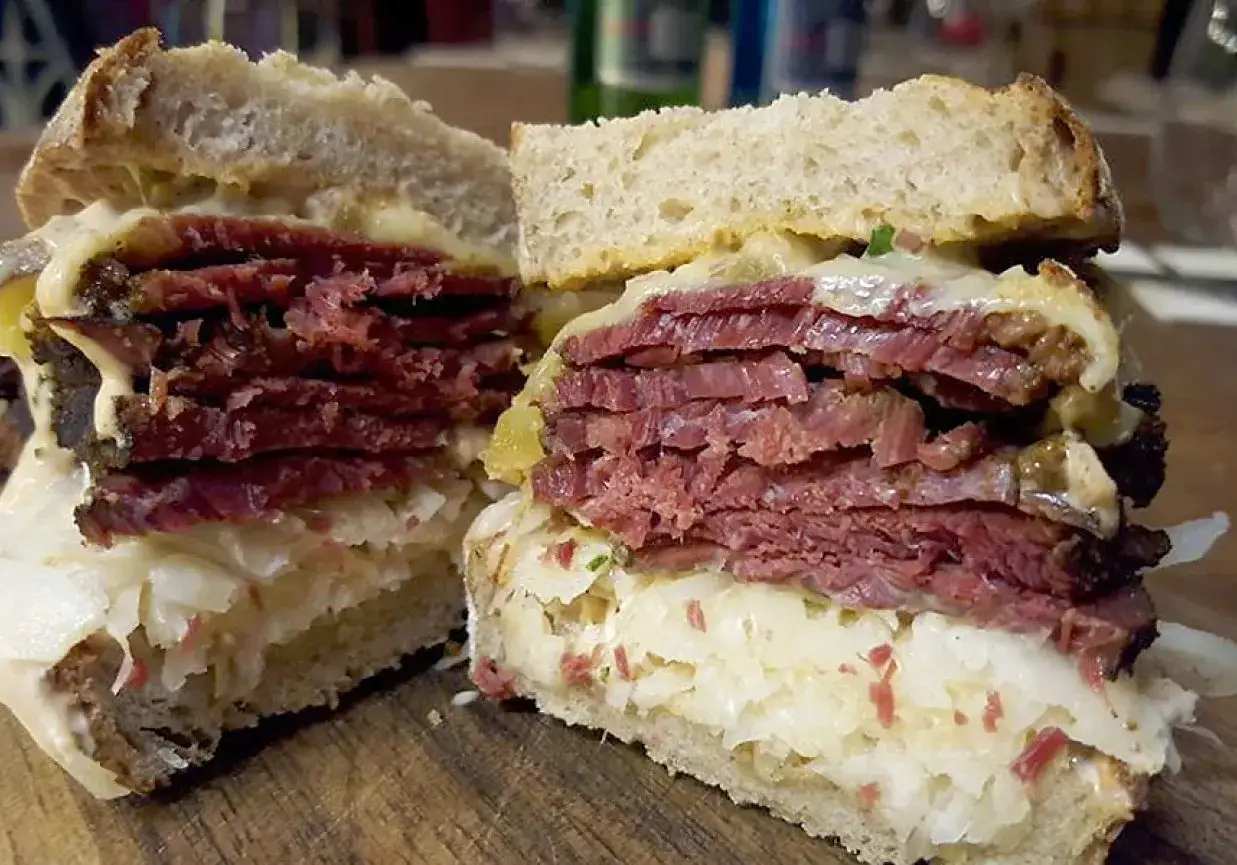 Pyszna kanapka z pastrami, z grubymi plastrami mięsa, kiszoną kapustą i serem, na chrupiącym pieczywie.