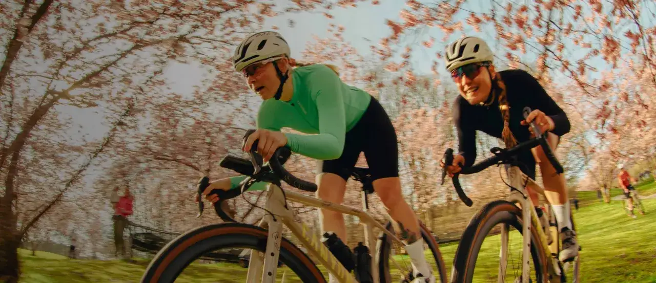 Dwie kobiety na rowerach ścigają się wśród kwitnących wiśni. Zwróć uwagę na dopasowanie roweru do sylwetki i terenu, by czerpać radość z jazdy.