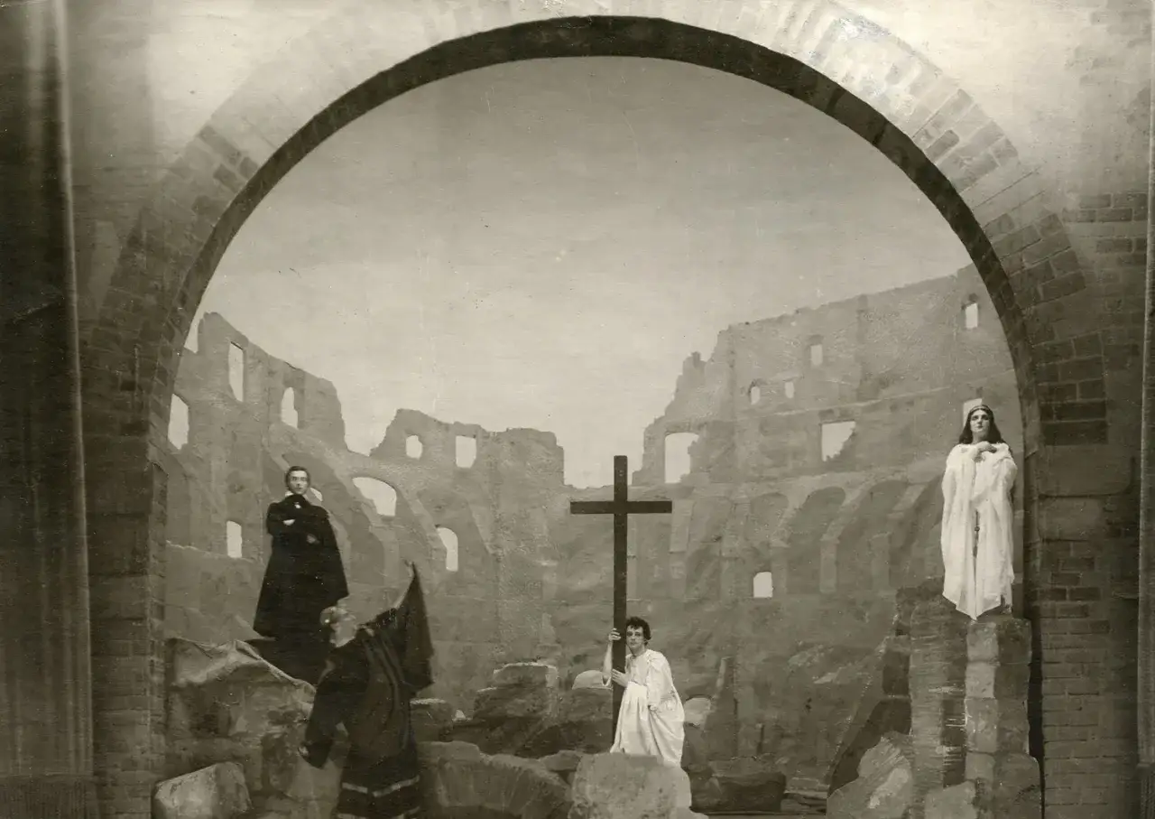 Scena teatralna z krzyżem i postaciami w ruinach. Szyfman, reżyser teatralny, stworzył dramatyczny obraz.