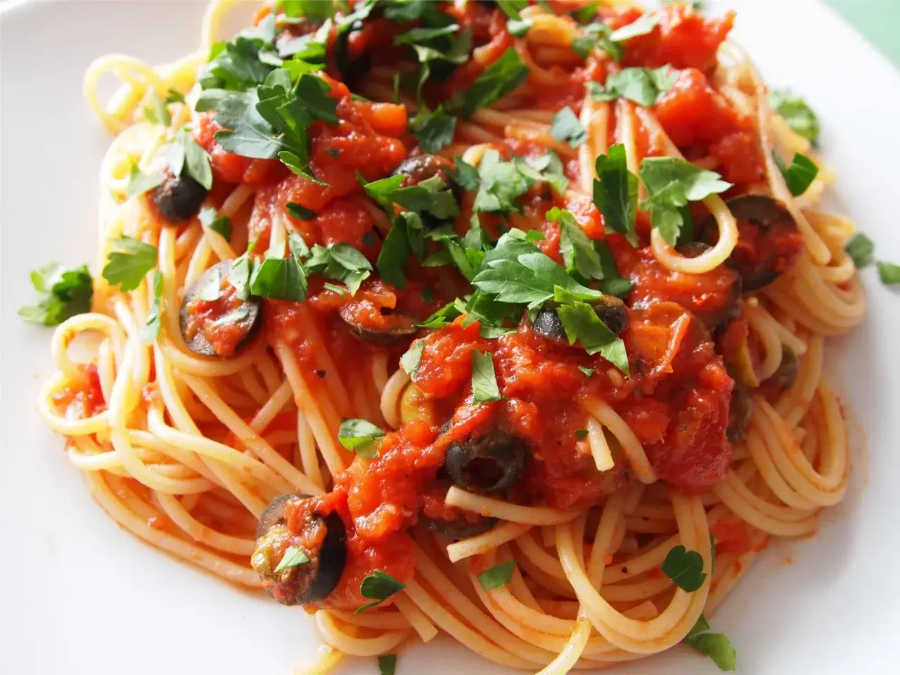 Pyszne Spaghetti Puttanesca przepis: makaron z sosem pomidorowym, czarnymi oliwkami i natką pietruszki.