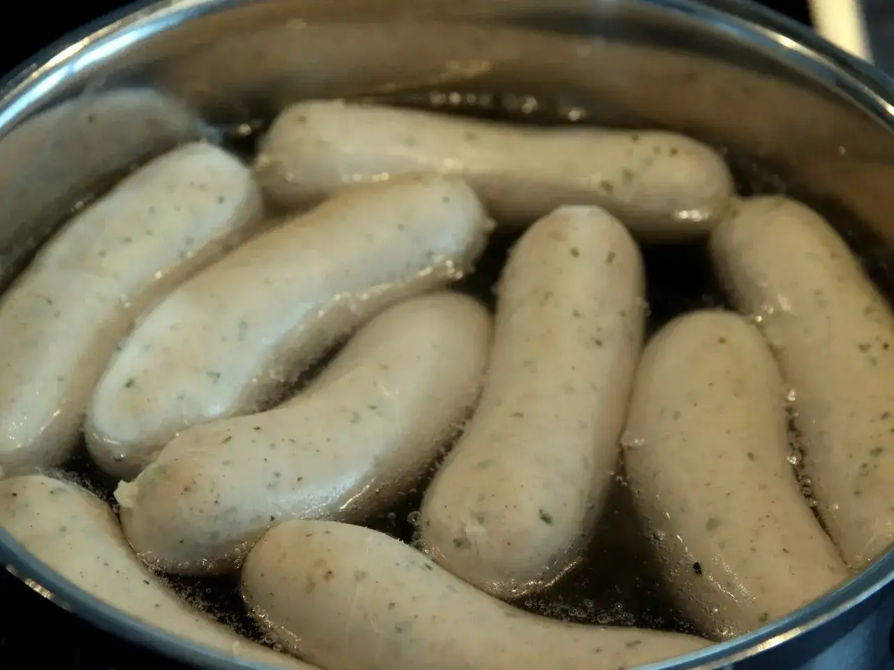 Białe kiełbaski gotują się w garnku. Zastanawiasz się, ile parzyć kiełbasę, by była idealna?