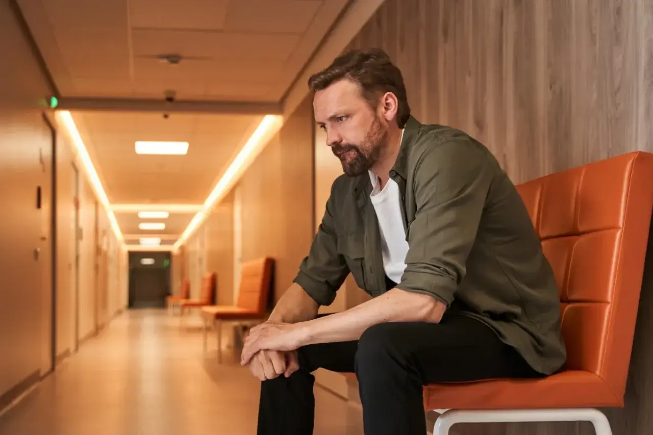 Mężczyzna w poczekalni, zastanawiający się nad andropauzą w jakim wieku może się pojawić.