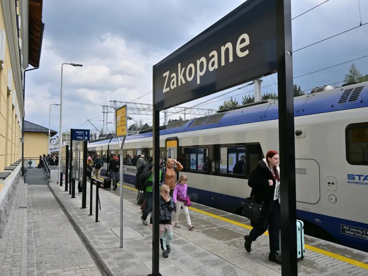 Ludzie wsiadają do pociągu do Zakopanego. Na peronie widać tablicę z napisem 