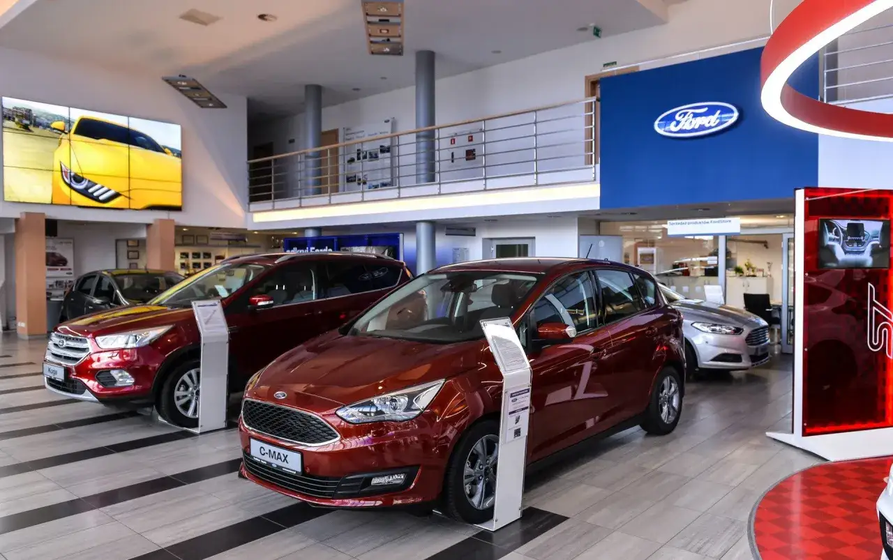 Salon Forda z czerwonym C-Maxem na pierwszym planie. Dowiedz się, jak negocjować cenę samochodu w salonie, by kupić wymarzone auto.