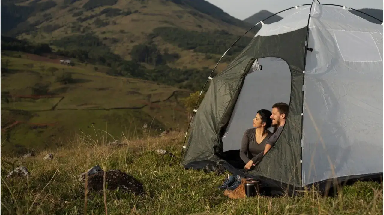 Para jak zabezpieczyć namiot przed deszczem, siedzą w namiocie na tle g&oacute;rskiego krajobrazu.
