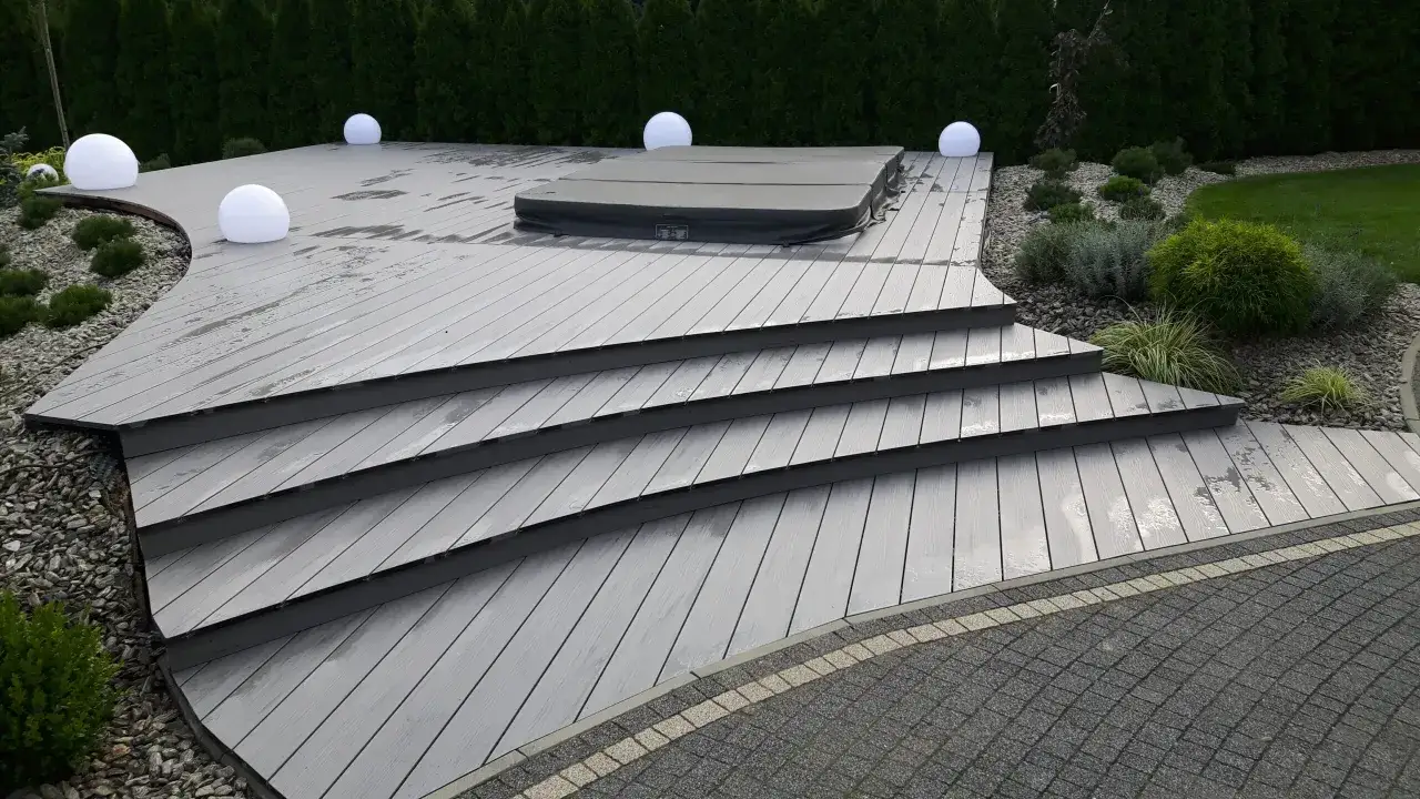 Nowoczesny taras z kompozytu, z jacuzzi i kulistymi lampami. Idealne rozwiązanie, czym wyłożyć taras tanio i efektownie.