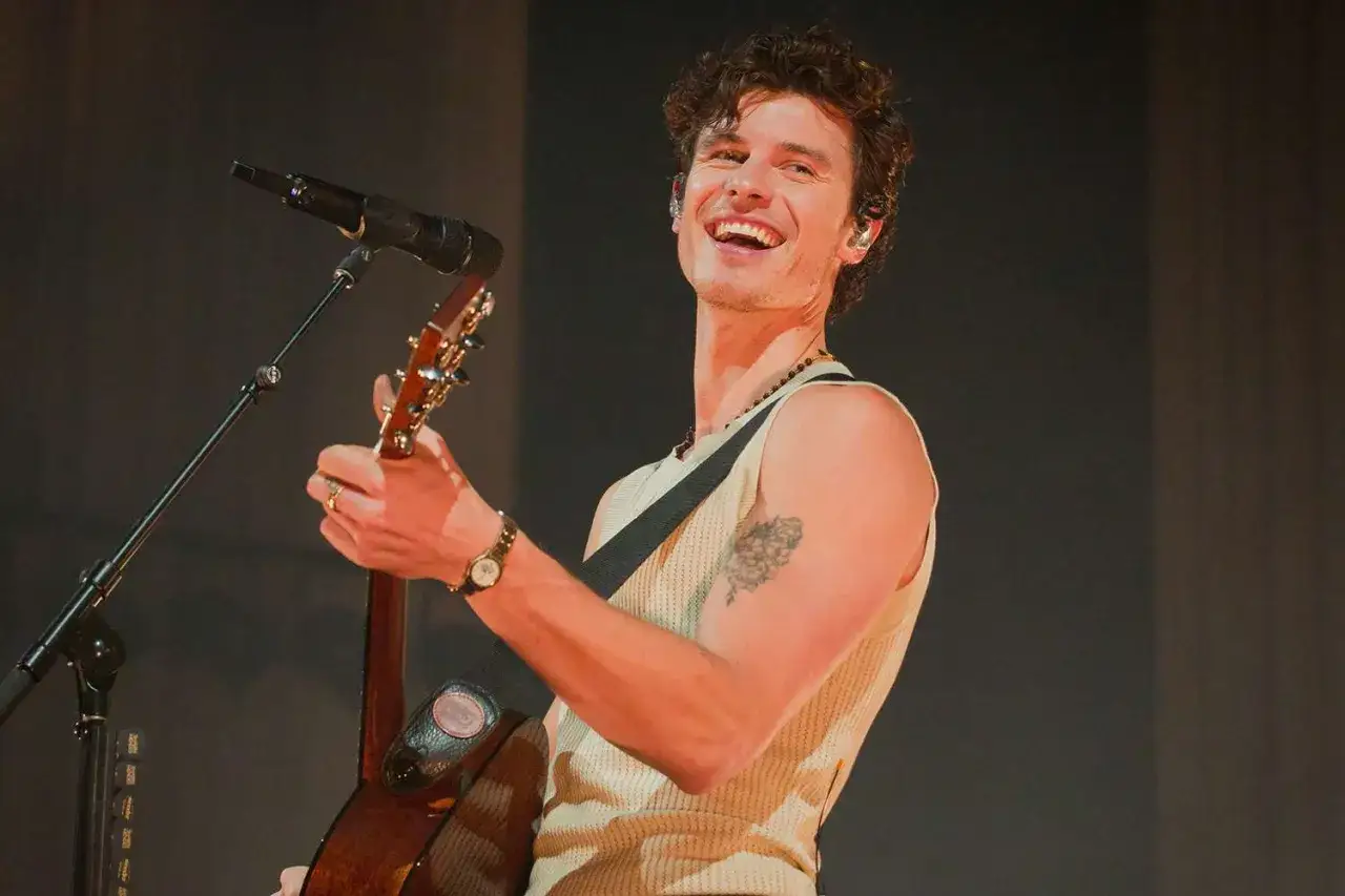 Shawn Mendes śpiewa i gra na gitarze, wykonując swoje utwory na koncercie.