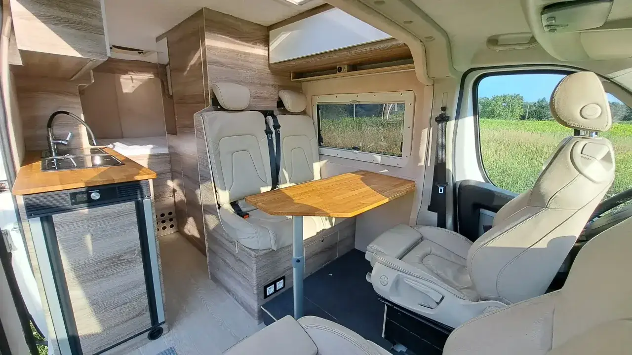 Wnętrze nowoczesnego busa kampera z wygodnymi fotelami, aneksem kuchennym i stołem. Idealny na podróże!