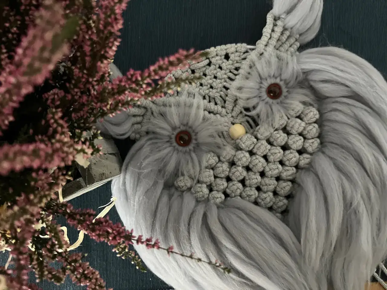 Szara makrama na kole w kształcie sowy. Wzory z frędzli i koralików tworzą jej pióra i oczy.