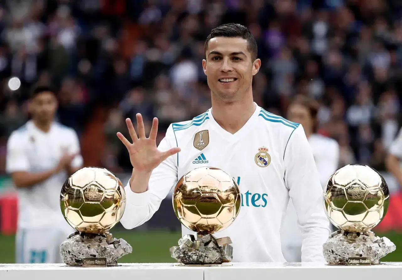 Cristiano Ronaldo, który zdobył Złotą Piłkę, pozuje z trzema trofeami.