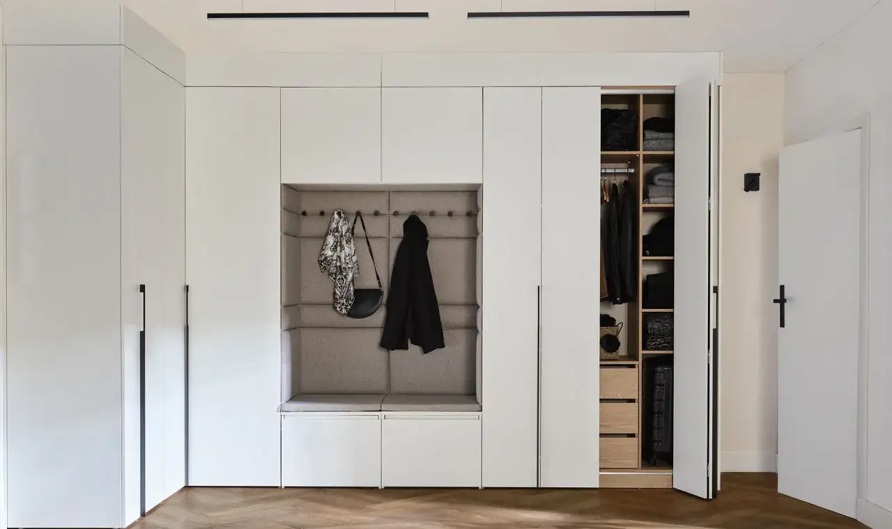 Nowoczesna zabudowa wnęki w przedpokoju z siedziskiem, wieszakami i otwartą garderobą.
