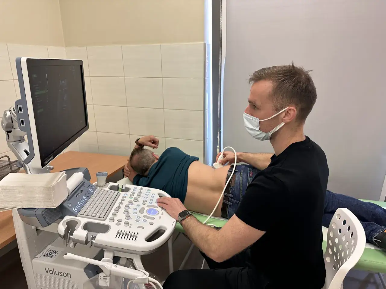 Urolog wykonuje badanie USG, pokazujące jak wygląda badanie prostaty. Pacjent leży na boku, lekarz używa sondy.