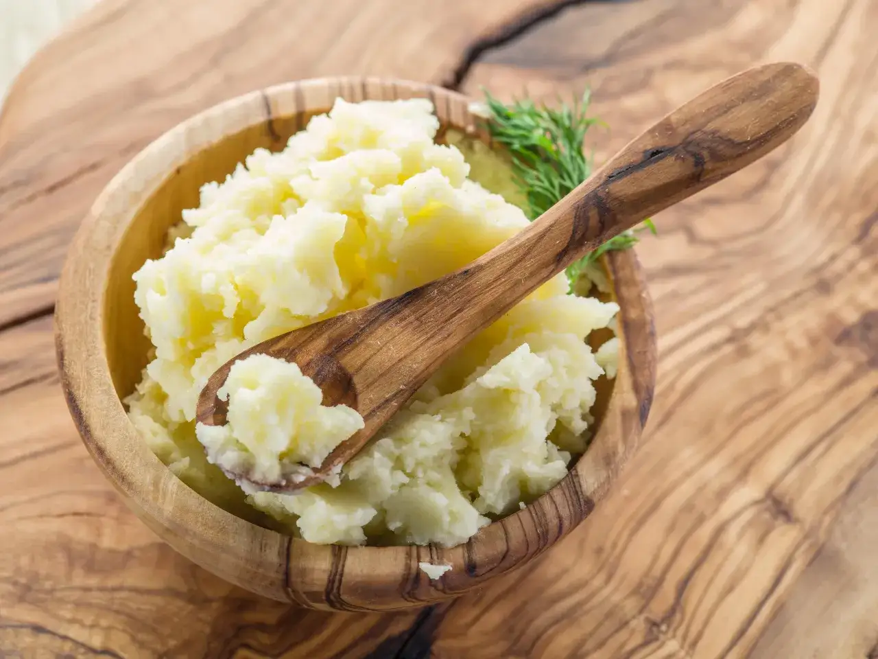 Puszyste puree ziemniaczane w drewnianej misce, z gałązką koperku i drewnianą łyżką. Idealne, by dowiedzieć się, jak zagęścić puree.