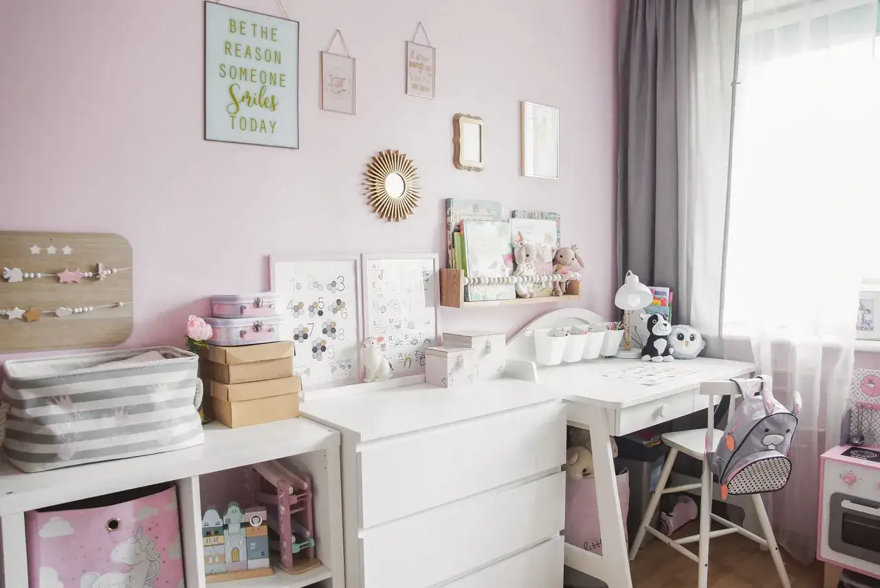 Uroczy mały pokój dziecięcy w bloku. Różowe ściany, biurko, regały z zabawkami i książkami, dekoracje ścienne.