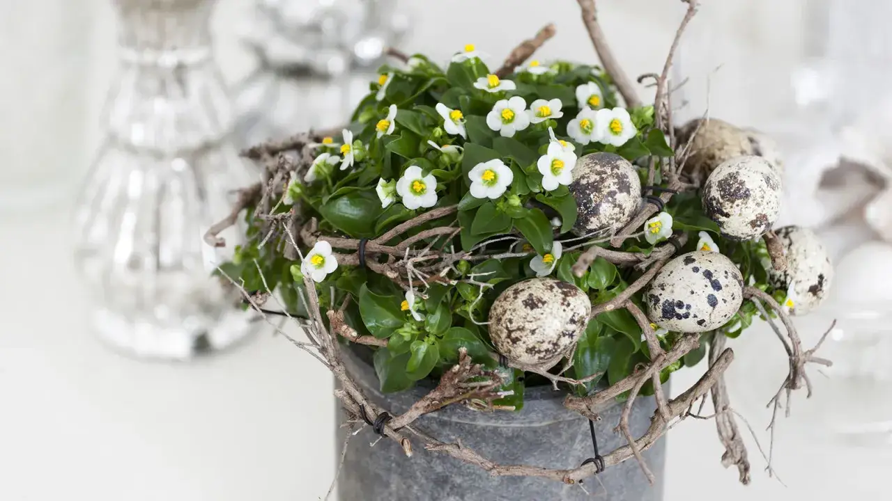 Wielkanocne kwiaty w donicy ozdobionej gałązkami i przepi&oacute;rczymi jajkami.