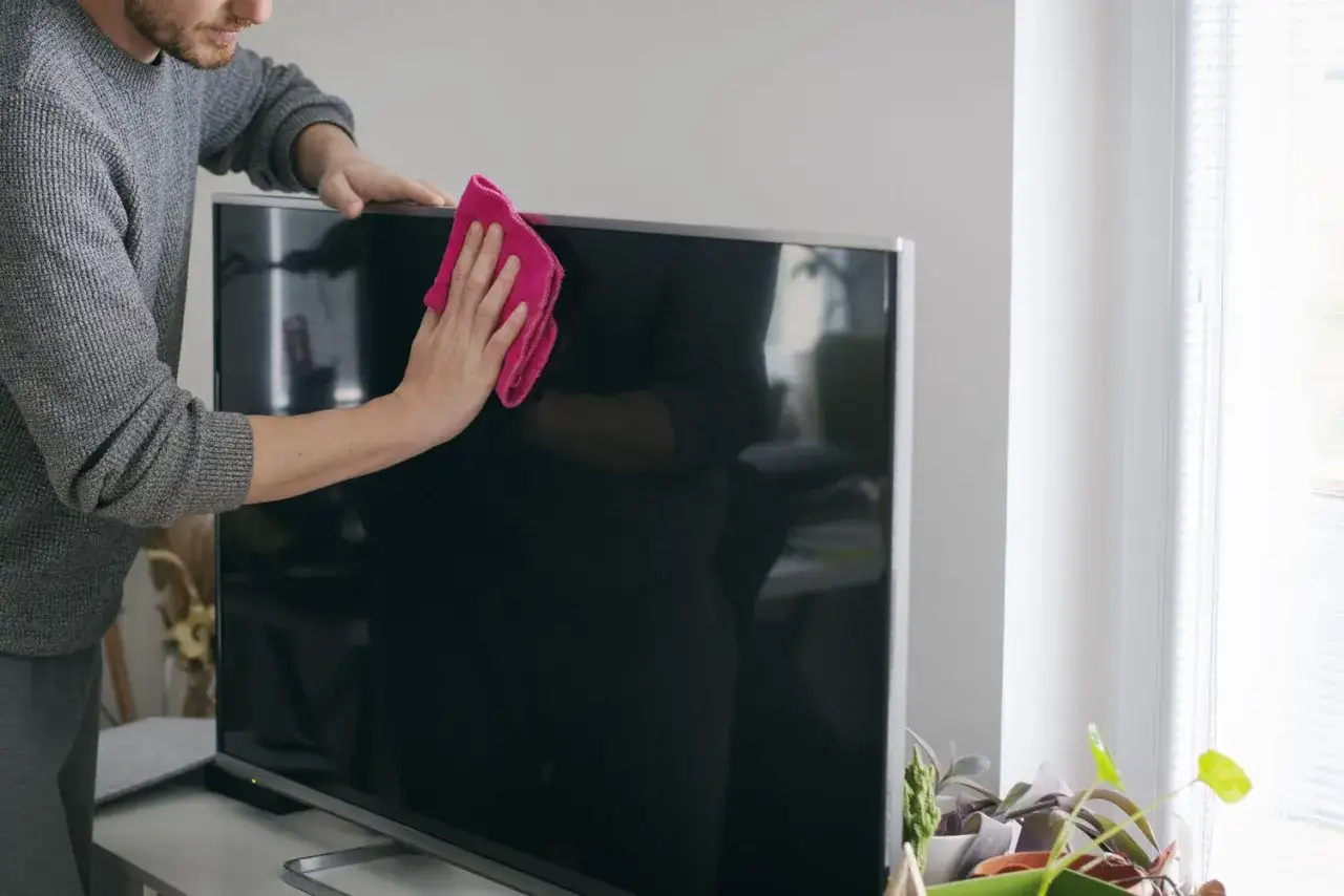 Mężczyzna delikatnie czyści ekran telewizora różową ściereczką z mikrofibry. To prosty sposób, czym umyć ekran telewizora, by był lśniący.