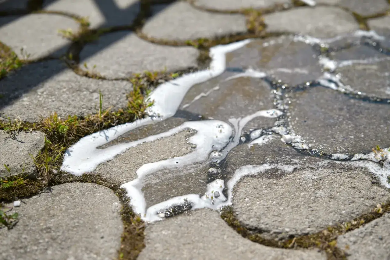 Piana i woda spływają po kostce brukowej, usuwając mech.