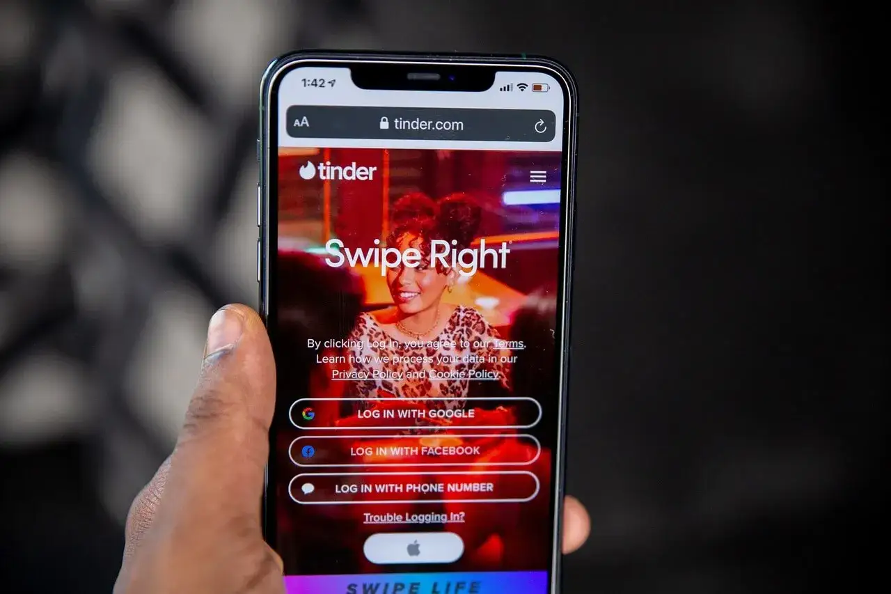Telefon wyświetla stronę logowania Tindera. Widoczne są opcje logowania przez Google, Facebook i numer telefonu, a także hasło 
