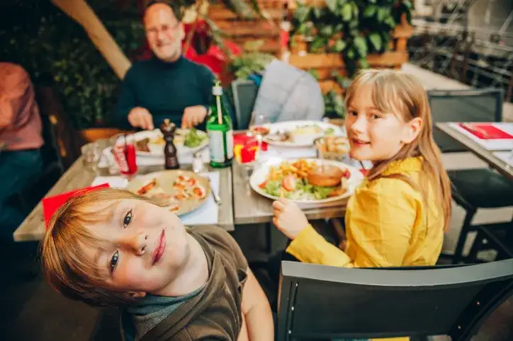 Rodzina z dziećmi jedząca obiad w restauracji z placem zabaw
