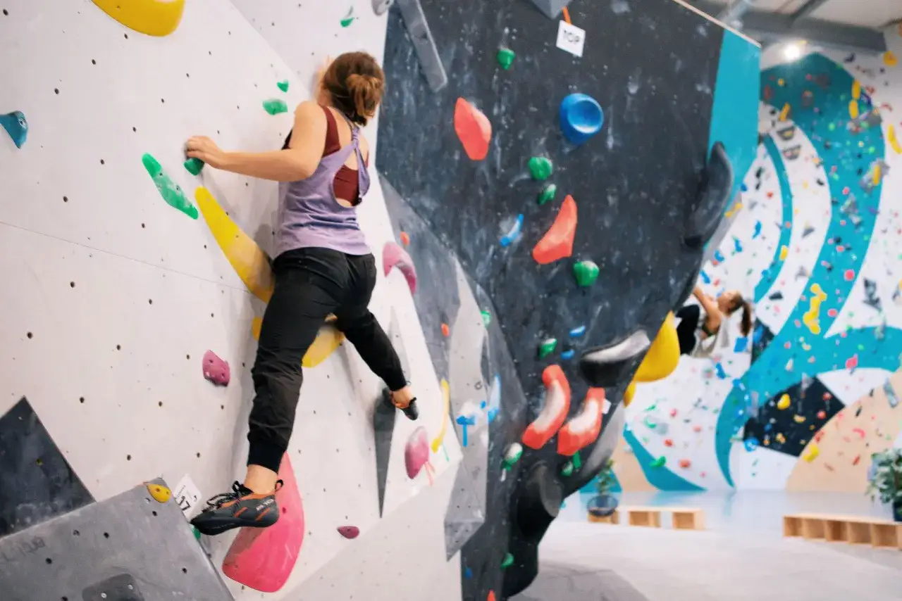 Dziewczyna wspina się po ścianie, używając specjalnych butów. Wspinaczka wymaga odpowiednich butów na ściankę wspinaczkową.