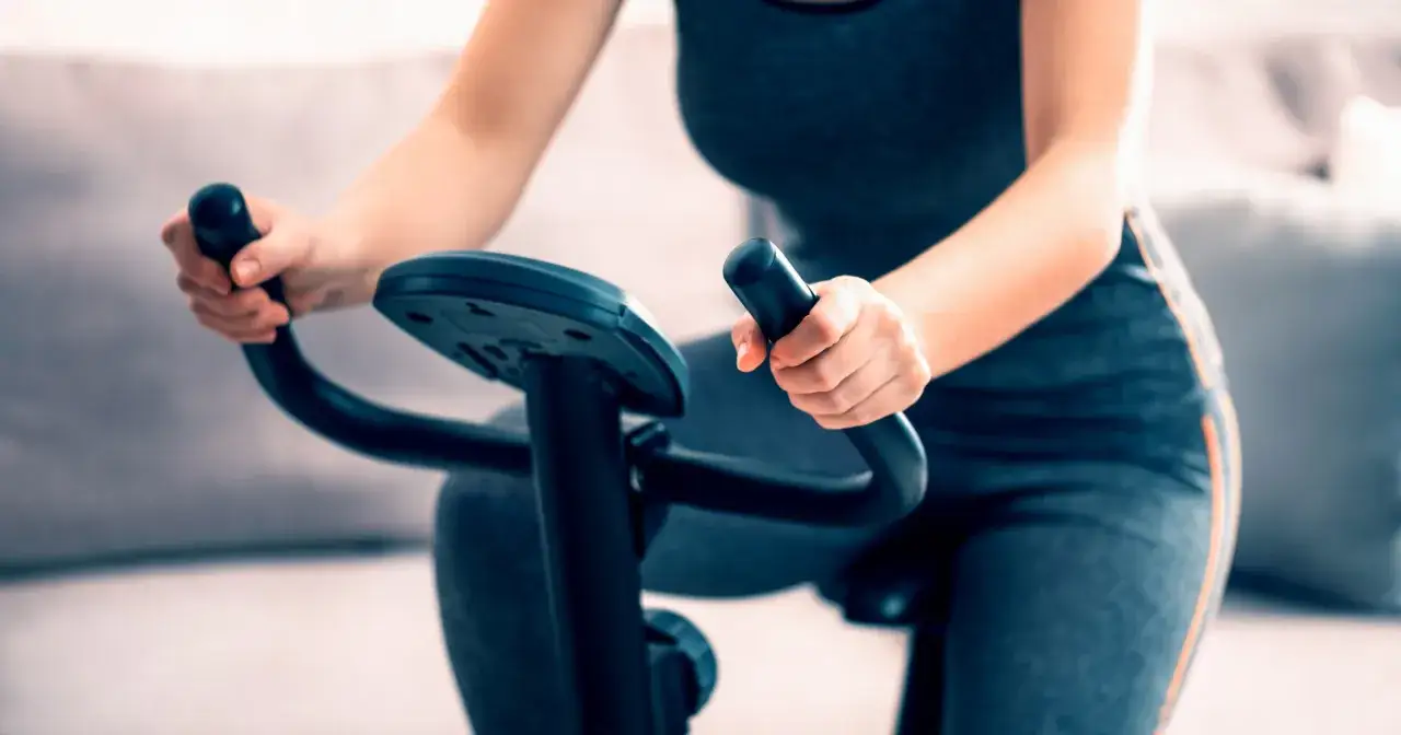 Kobieta ćwiczy na rowerze stacjonarnym, co jest świetnym sposobem, by sprawdzić, czy na rowerze stacjonarnym można schudnąć.
