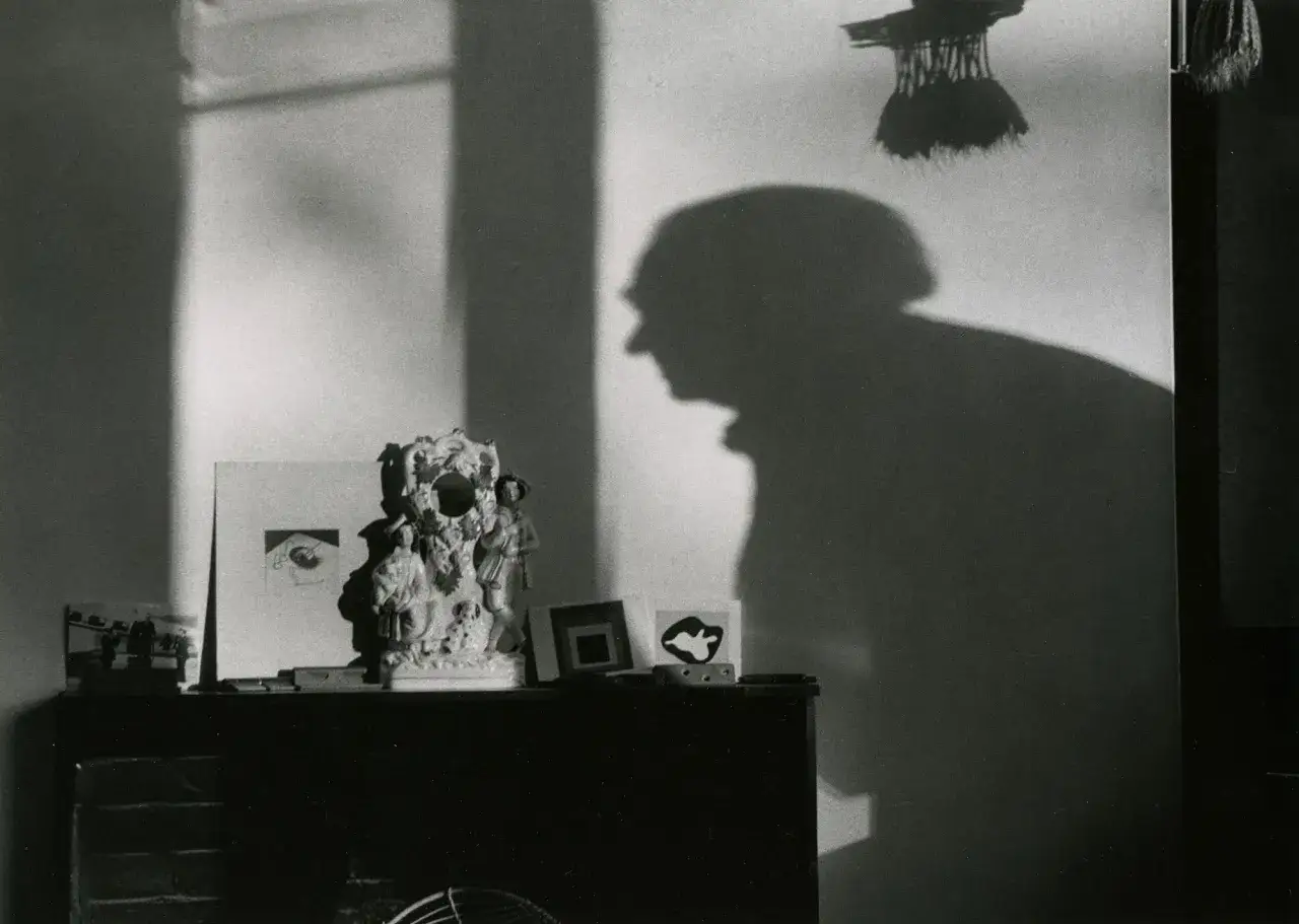 Cień Andre Kertesz na ścianie, obok ozdobnej figurki i przedmiot&oacute;w na kominku.