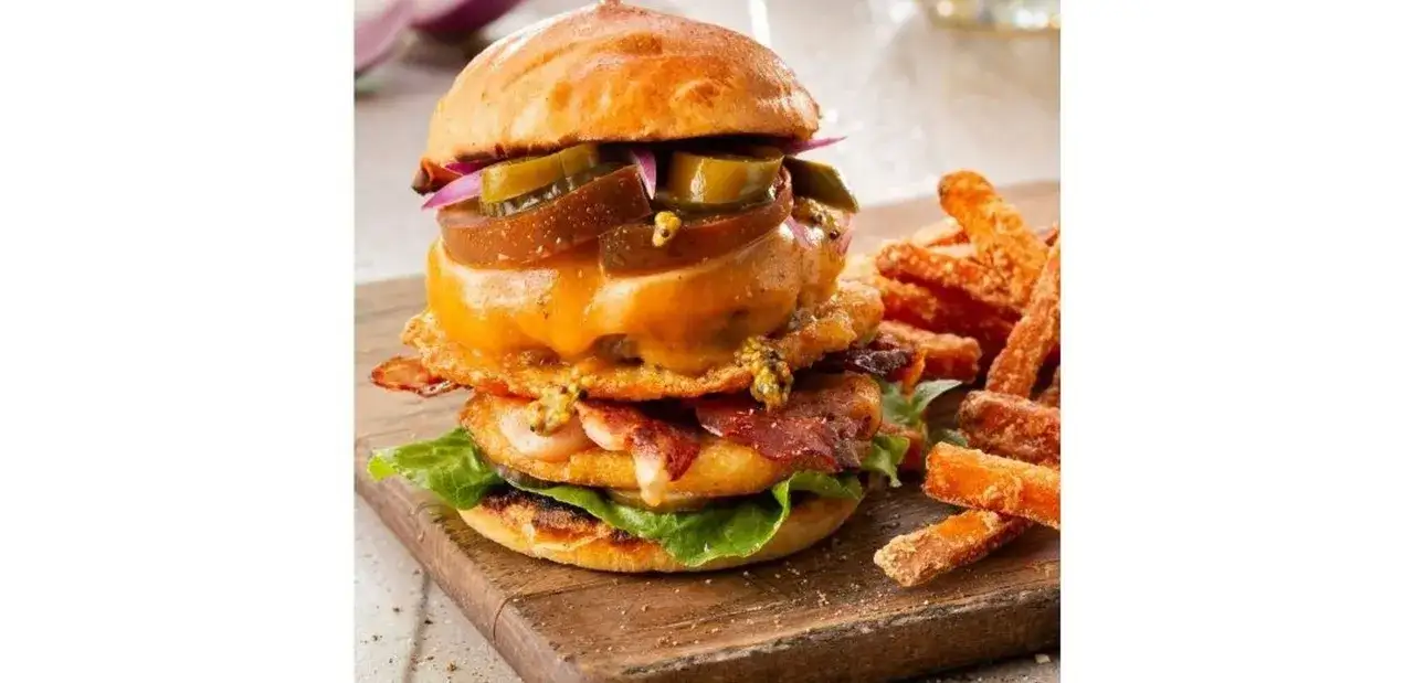 Pyszny burger drwala przepis: soczysta wołowina, ser, bekon, pikle i chrupiące frytki z batat&oacute;w na drewnianej desce.