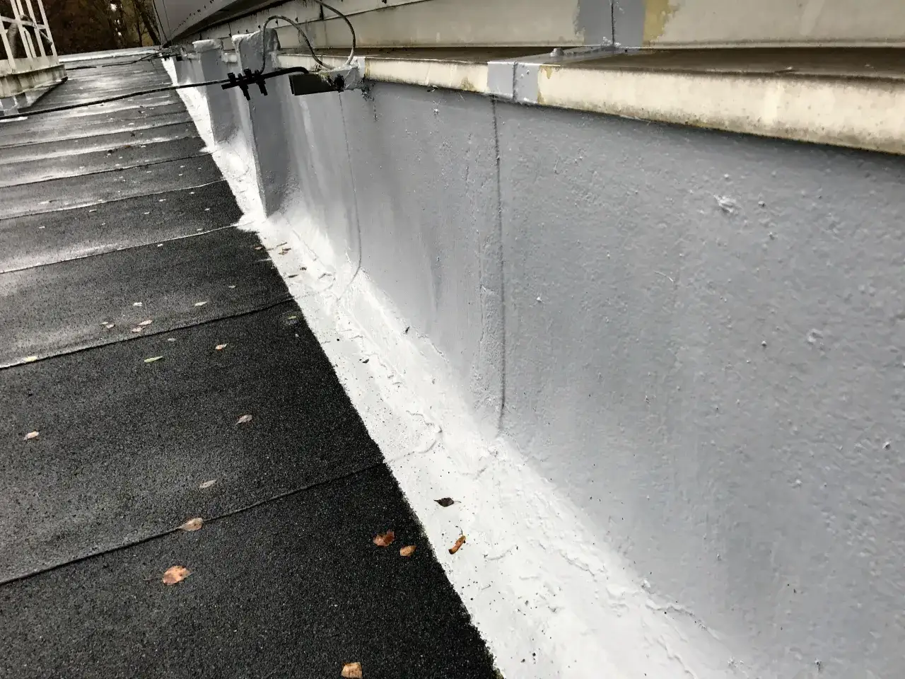 Szara ściana i czarny dach z liśćmi. Widoczne ślady uszczelniania dachu.