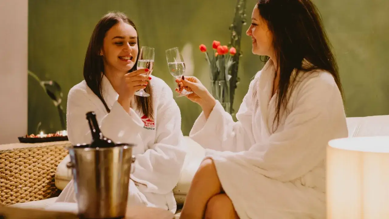 Dwie kobiety w szlafrokach wznoszą toasty kieliszkami szampana. Idealny weekend na Dzień Kobiet w spa.