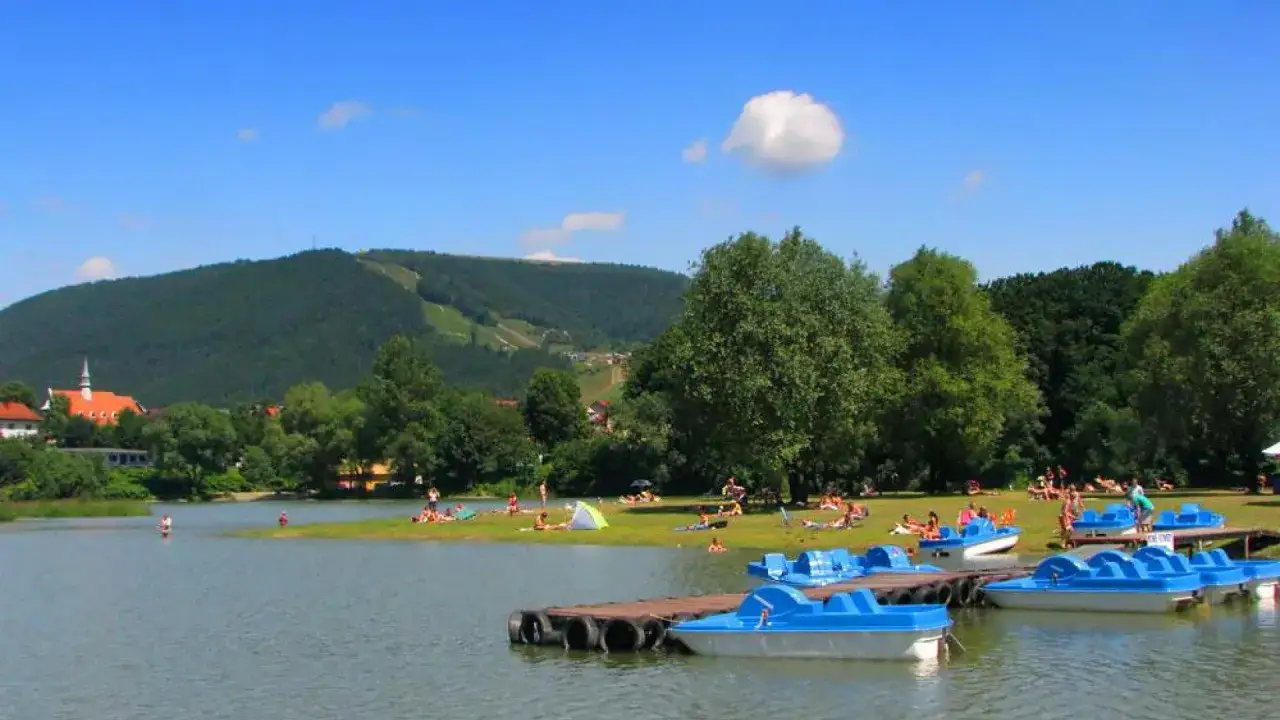 Jezioro Żywieckie oferuje liczne atrakcje: plażowanie, kąpiele i rejsy rowerami wodnymi. W tle g&oacute;ra z trasami narciarskimi.