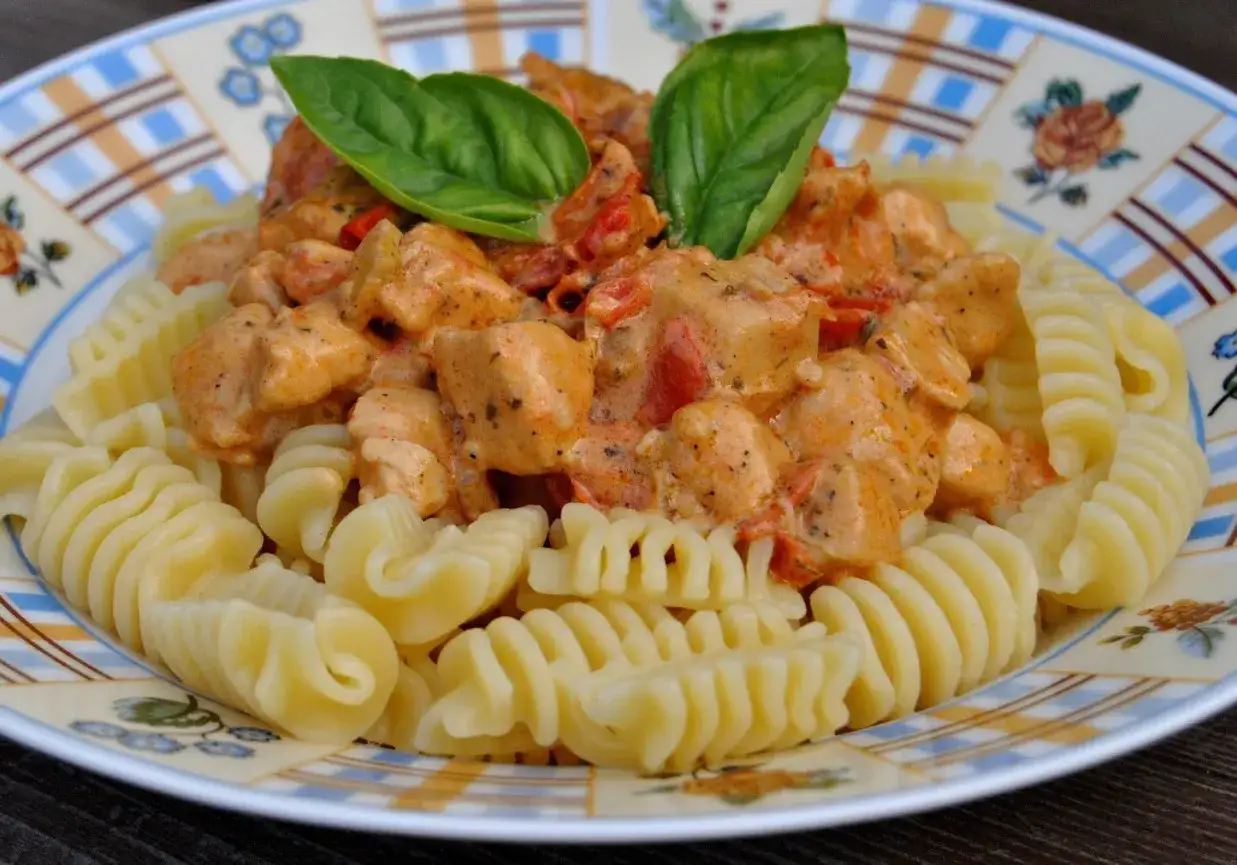 Pyszny makaron fusilli z kurczakiem w kremowym sosie paprykowym, udekorowany listkami bazylii.