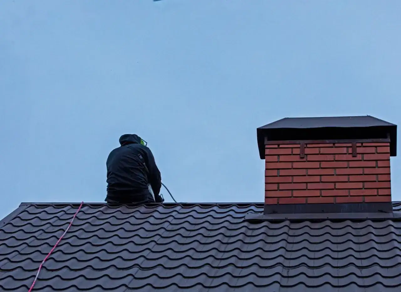 Osoba na dachu czyści komin. Dowiedz się, jak wyczyścić komin domowym sposobem, by zapewnić bezpieczeństwo i efektywność ogrzewania.