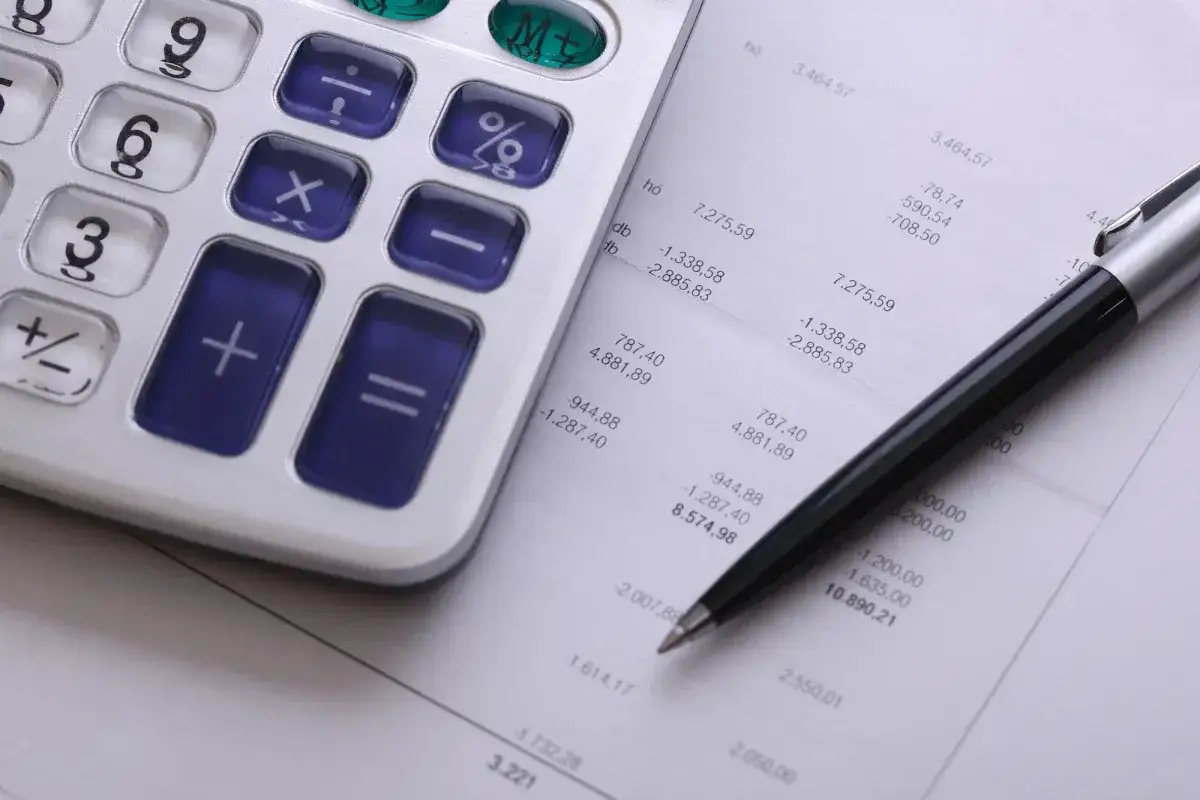 Kalkulator i długopis na arkuszu z danymi finansowymi. Zastanawiasz się, ile kosztuje windykacja należności?