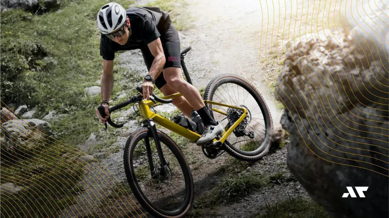 Kolarz na żółtym rowerze typu gravel pokonuje kamienisty, górski szlak, wzbijając tumany kurzu.