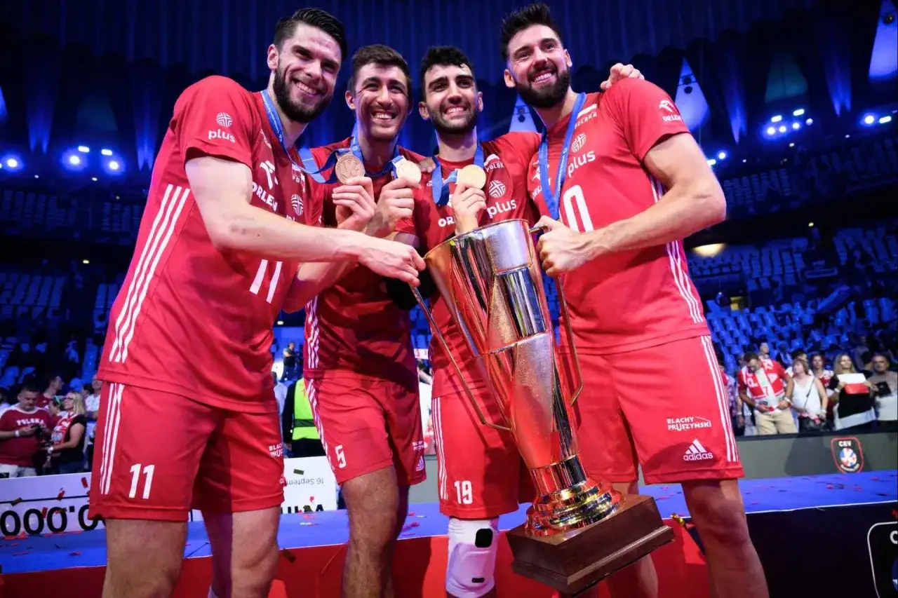 Siatkarze w czerwonych strojach z pucharem i medalami. Polska drużyna świętuje zwycięstwo, co z pewnością odzwierciedli **mistrzostwa świata siatkówka tabela**.